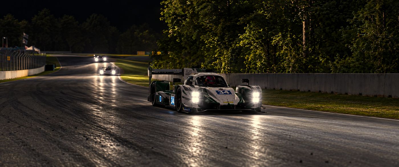 El LMP2 número 34 de Xallas MotorSport de frente, con los faros encendidos, sobre el asfalto mojado de Road Atlanta y dos coches detrás.